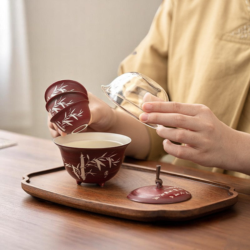 Person holding three red teacups with white bamboo patterns on a wooden tray.