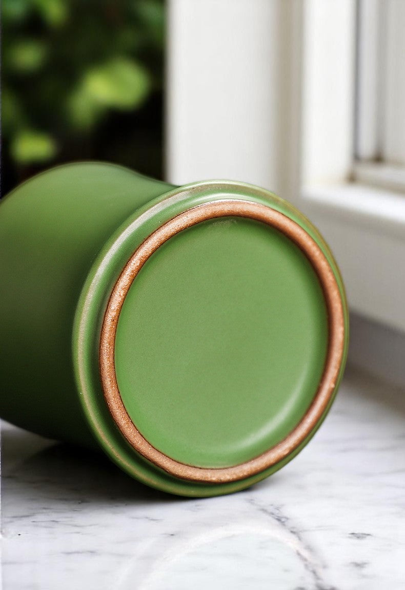 Green ceramic cup with brown rim at the bottom on a marble surface