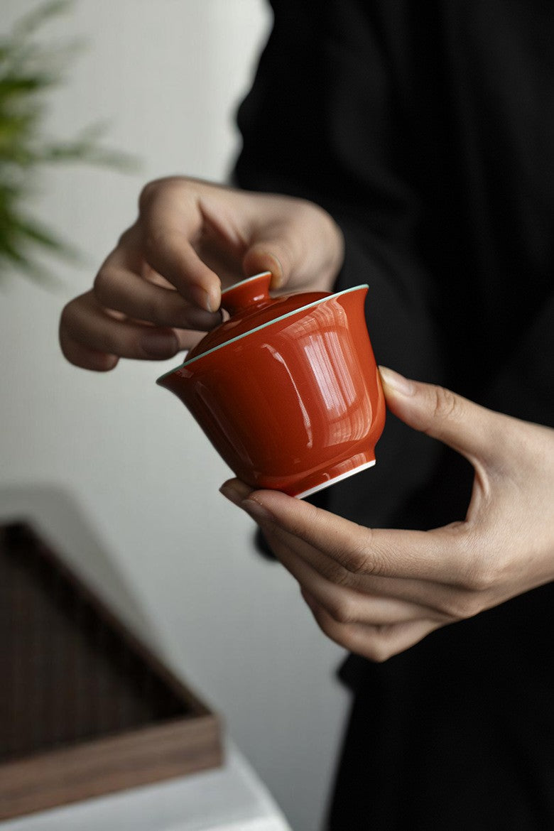 Holding vibrant orange ceramic gaiwan for solo gongfu tea session