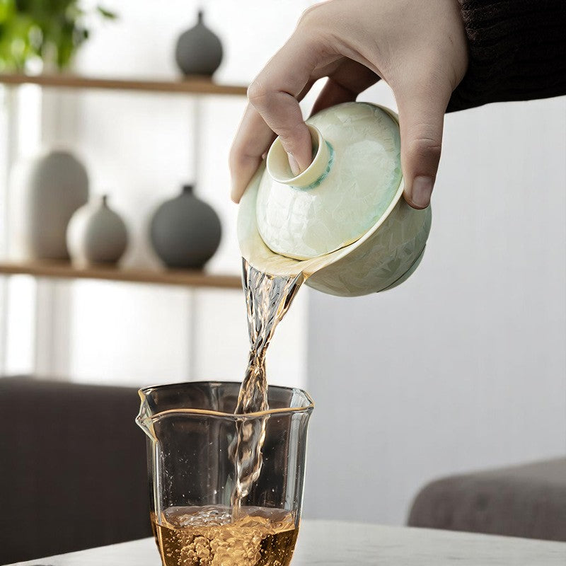 Pouring tea from yellow-green gaiwan with luminous glaze in ritual setting