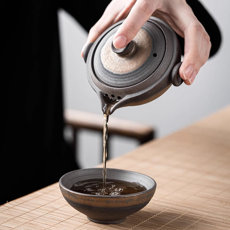 Pouring tea from stoneware teapot into matching ceramic tea bowl