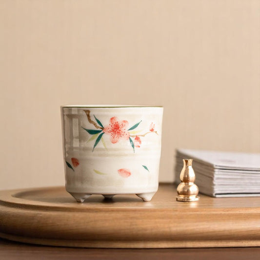 Ceramic pot with peach blossom design on a wooden surface with a beige background