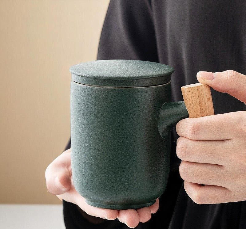 Holding forest green ceramic mug with wooden handle, cozy setup
